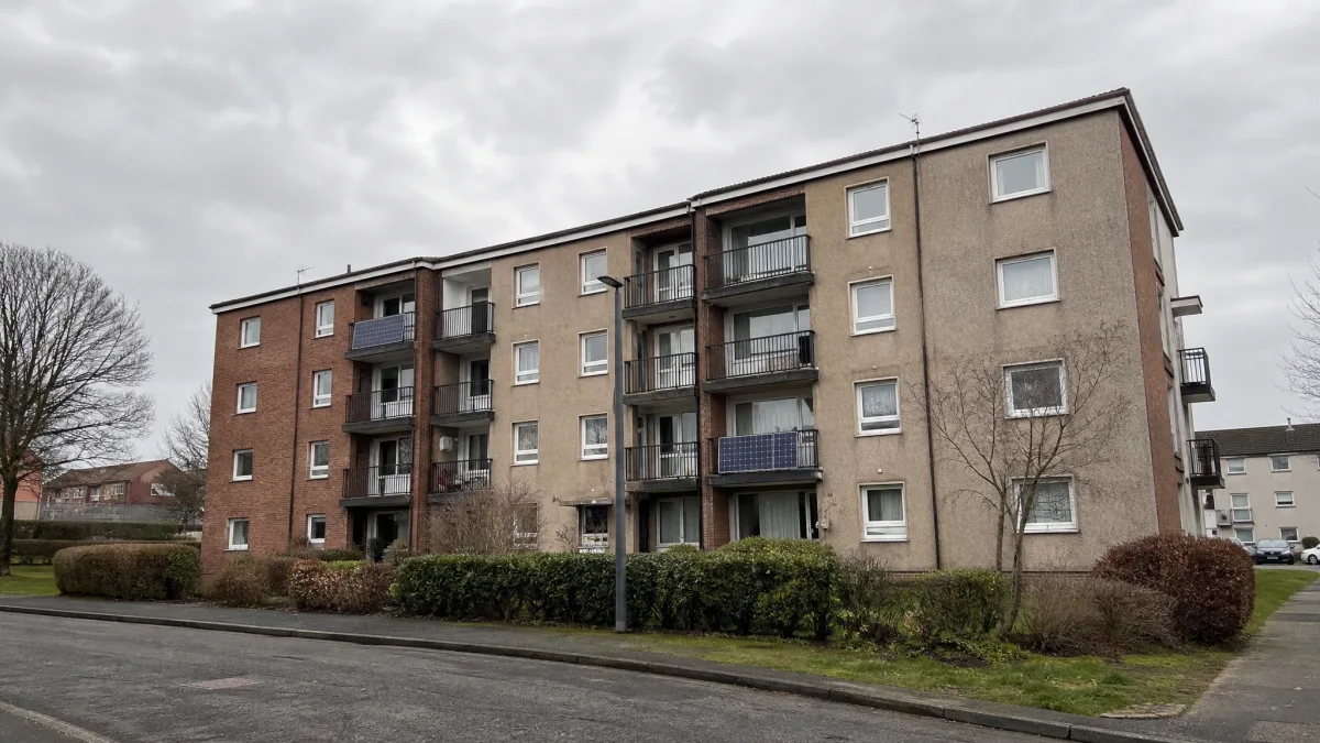 A British apartment block with a mix of balconies, some with small solar panels visible, under an overcast sky.